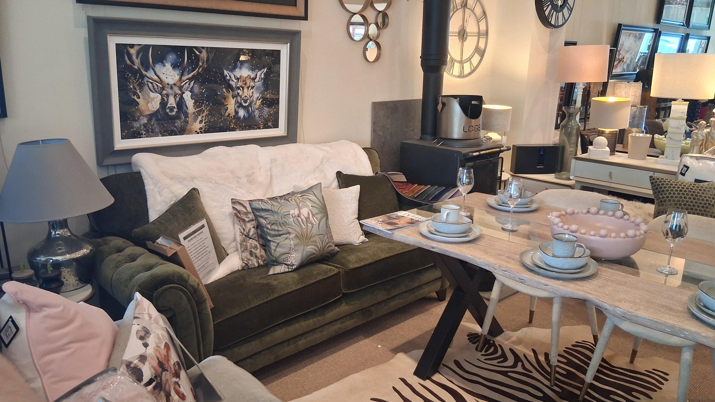 Green velvet Duxford sofa next to a woodburning stove with dining table set for two